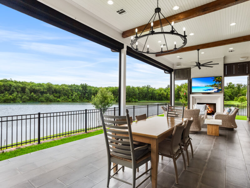 Covered outdoor living area with dining space, fireplace, and panoramic lake views at a custom home in The Preserve at Harveston.