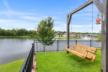 Wooden porch swing overlooking the lake behind a custom home in The Preserve at Harveston, Baton Rouge.
